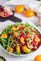 Fruit vitamin salad of pomegranate, tangerine, arugula and pumpkin seeds in a plate on the table. Organic vegetarian food.  Vertical view. Close-up