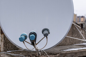 Set of satellite converters on blurred background of roof and white receiving dish