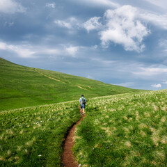 Fototapeta premium Back view hiker man with backpack going at hilly terrain natural mountain enjoy adventure
