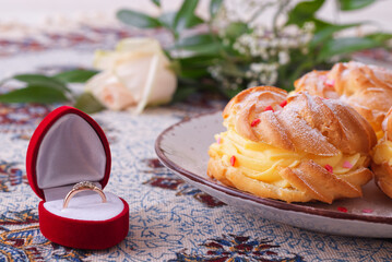 Low angle close-up of a golden ring, dessert and flower, romantic Valentine atmosphere, engagement or birthday.