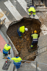trabajadores arreglando una tubería en la ciudad y excavando un gran agujero para descubrir la...