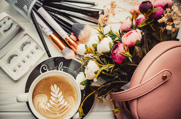 Cup of coffee and makeup brushes on wood white background with handbag and flowers