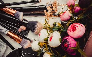 Makeup brushes on wood white background with flowers