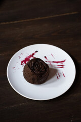 a chocolate cupcake lies on a white plate with jam on the background of a wooden table in a cafe