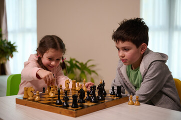 Kids having great time together playing chess. Brother teaching his younger sister playing chess...