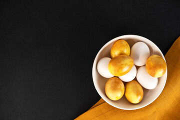 Yellow Easter eggs in a bowl on a dark background. Natural duing Easter eggs with turmeric powder in yellow color.