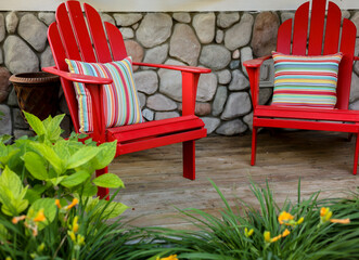 Stargazer asiatic lilies and the cherry red adirondack chairs against a fieldstone wall create a...
