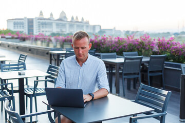 Successful young male businessman working with laptop on vacation. He wears a shirt and white shorts. Work outside the office, freelancer