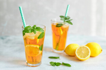 Fototapeta premium Iced iced tea in a glass with a straw, mint leaf and lemon slices inside. Cool drinks in the heat