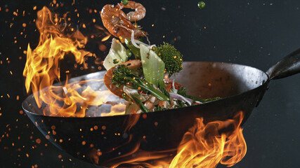 Freeze Motion of Wok Pan with Flying Ingredients in the Air and Fire Flames. - obrazy, fototapety, plakaty