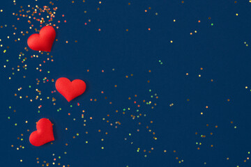 Festive background with red hearts and small multicolored holographic sparkles on dark blue...