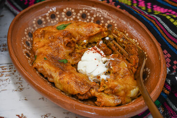 Bean enchiladas served in traditional cast iron skillet and clay dishes, white wooden table