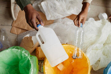 Top view close up of African-American father and son putting plastic in recycling bins at home,...