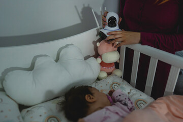 unknown woman mother adjusting and setting up Surveillance security camera on baby bed at home in...