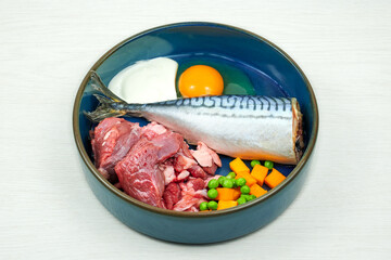 Natural raw dog food. Fresh raw meat, fish and vegetables in bowl on grey background.