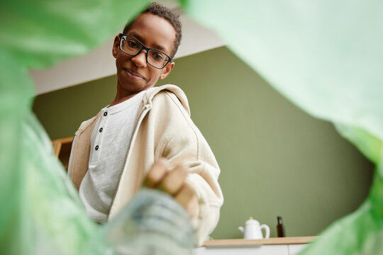 Low angle view at African-American boy sorting household waste at home, recycling bin POV - Powered by Adobe