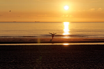 Silhouette of a woman standing in yoga pose on the Texel beach during sunset. Caucasian girl...