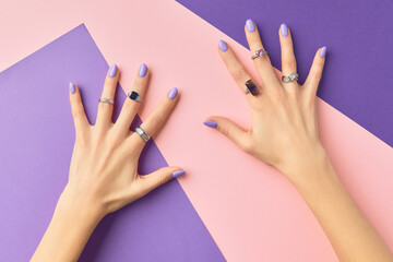 Beautiful womans hands in with purple fashionable spring nail design on pink purple background