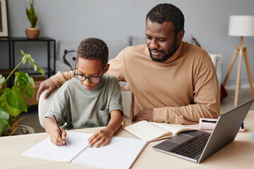 Portrait of African-American father helping son with homeschooling while studying at home, copy...