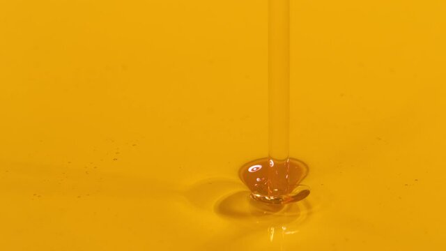 SLOW MOTION MACRO, DOF: Golden liquid falls into a container full of cold pressed extra virgin olive oil. Shiny unrefined avocado oil streams into a full dish. Organically grown cooking ingredient.