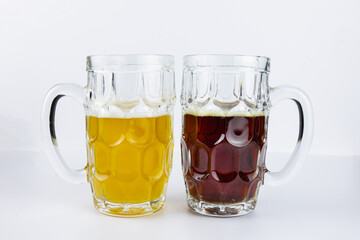Two glass beer mugs with light and dark beer on white surface