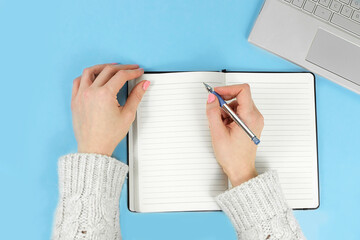 top view of female hands writing in a notepad on blue background with laptop