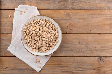 Dry raw cicerchia or indian pea on a ceramic plate with napkin on natural wooden background, top view, copy space. Legumes known as Lathyrus Sativus, Chickling Vetch, Blue Sweet Pea, made in Puglia