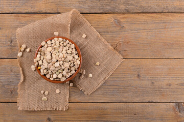 Dry raw cicerchia or indian pea on a clay plate with burlap napkin on natural wooden background,...