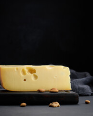 triangular piece of maasdam cheese on a brown wooden board