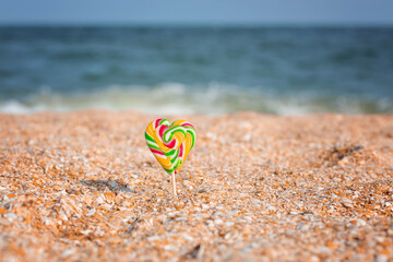 Obraz premium Closeup colorful lollipop in heart shape on sand, flat lay view. Happy Valentines day concept