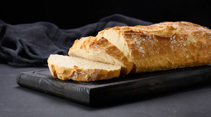 baked whole oval bread made from white wheat flour on a black table, fresh pastries