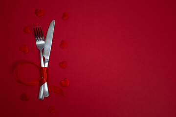 Valentines day meal background with red ribbon, hearts, fork, knife, white plate and napkin. Romantic holiday table setting. Beautiful background with blank. Restaurant concept. Flat lay