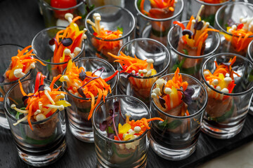 Light meat snack with Korean carrots, sprouted seeds and herbs in a glass cup.