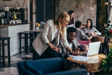 Black man works in cafe and discusses information from documents with woman
