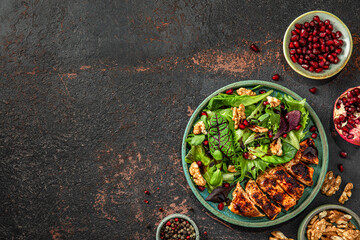 Salad with grilled chicken fillet, mix greens, walnuts, pomegranate and balsamic sauce on black background