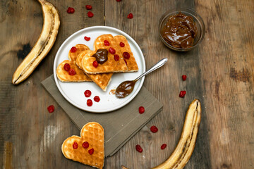 Homemade Belgian waffles heart shaped on plate with colorful red sweet cherry berries, banana, and boiled condensed milk, dessert food. background for Valentines day, womens day, love, romance