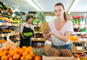 Young woman customer holding fresh pineapples in hands on the supermarket