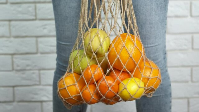 Plastic free shopper with fruits. An eco friendly woman hold a big string shopper with oranges and apples in the room.