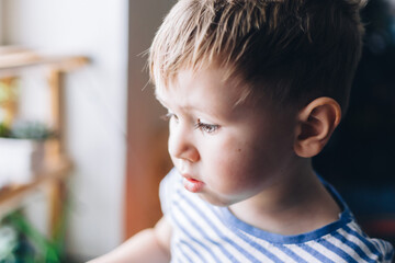 Caucasian boy watering from a yellow watering can home plants on the windowsill
