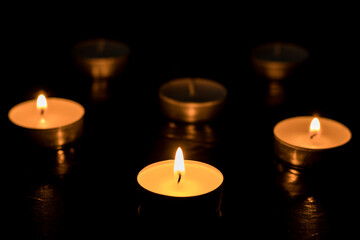 Three candles Burning out of six on dark table, black background, Memory day.