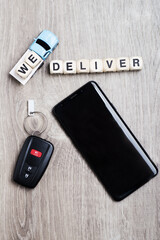 WE DELIVER. Composition from a toy truck and cubes on a gray table. Car keys and mobile phone.