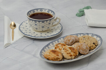 Close up shot of cup of red tea with plate full of wheat and oatmeal cookies on marble top and small black background.