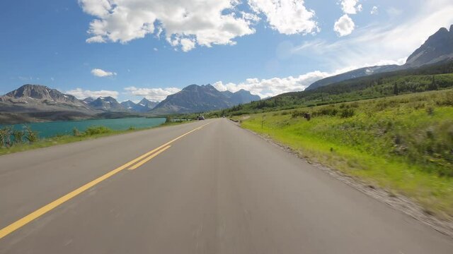 Driving a car on asphalt mountain road towards Glacier National Park in Montana. Sunny day with blue sky and white clouds	