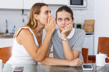 Young girl whispering to her best friend gossip in kitchen