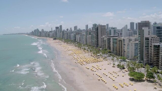 aerial view of the beach of Boa Viagem in Recife in the northeast region of Brazil with the sea buildings blue sky and beach umbrellas on the sand rotating from left to right advancing above the avenu