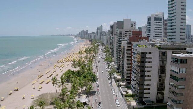 aerial view of Boa Viagem beach in Recife in the northeast region of Brazil with the sea buildings blue sky and umbrellas on the sand with camera advancing following the avenue with cars passing below