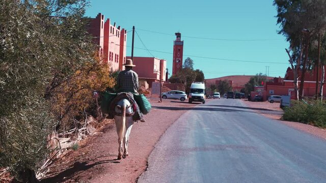 Man in straw hat riding on horse with luggage by walking pedestrian on road trip