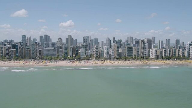 open plan aerial view of Boa Viagem beach in Recife in the northeast region of Brazil with the sea buildings blue sky and beach umbrellas on the sand with camera movement moving away from shore