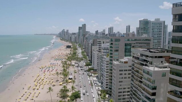 aerial view of the beach of Boa Viagem in Recife in the northeast region of Brazil with the sea buildings blue sky and umbrellas on the sand with movement passing close between the buildings until rea