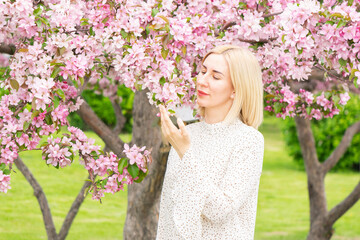 Fototapeta premium Young woman among the blossoming trees. Spring nature park or garden, flowering trees. Concept spring woman health